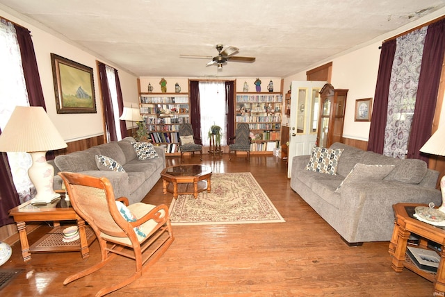 living area with a ceiling fan, a wainscoted wall, and wood finished floors