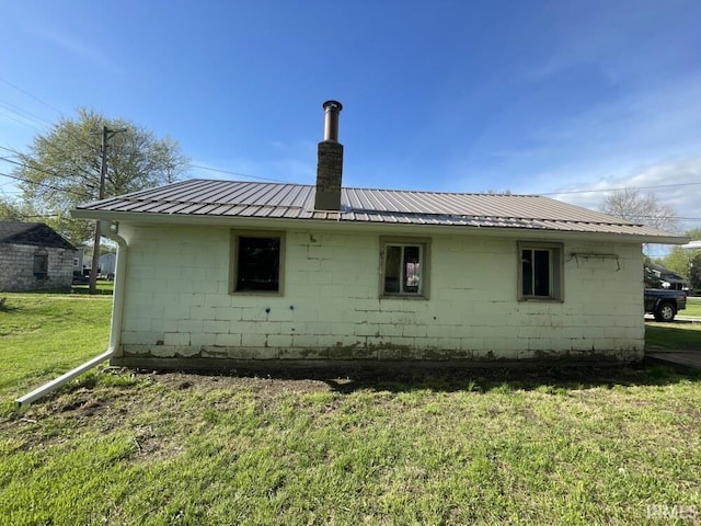 251 N Snowden St, Andrews, IN 46702 - view of home's exterior featuring concrete block siding, a chimney, metal roof, and a lawn