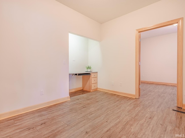 empty room featuring light wood-style flooring, baseboards, and a desk