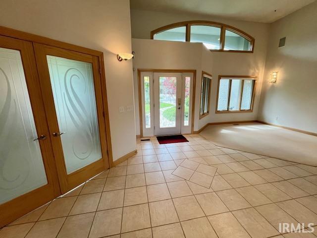 entrance foyer featuring french doors, light tile patterned floors, baseboards, a towering ceiling, and light carpet