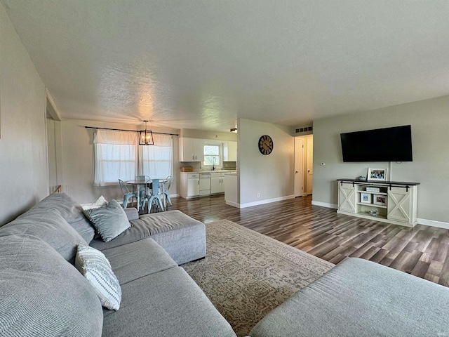 living area with dark wood finished floors, a textured ceiling, baseboards, and a chandelier