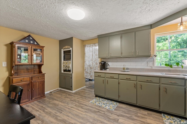kitchen with a sink, light wood-style flooring, tasteful backsplash, light countertops, and a textured ceiling