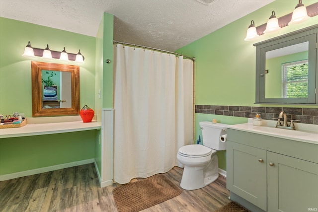 full bath with wood finished floors, a textured ceiling, vanity, toilet, and wainscoting