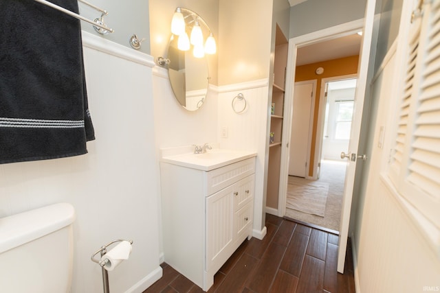 half bathroom with wood finished floors, toilet, vanity, and baseboards