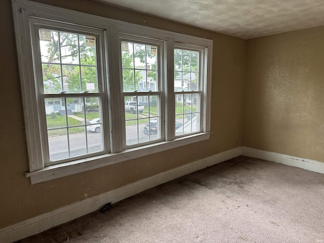 carpeted empty room featuring baseboards, a textured wall, and a textured ceiling
