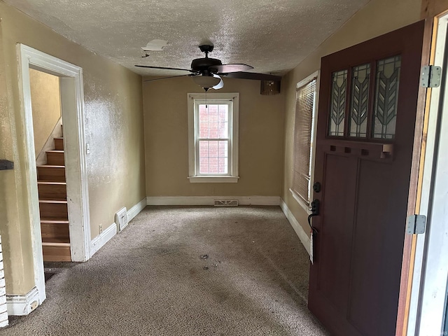 carpeted foyer entrance with a textured ceiling, baseboards, stairs, and ceiling fan