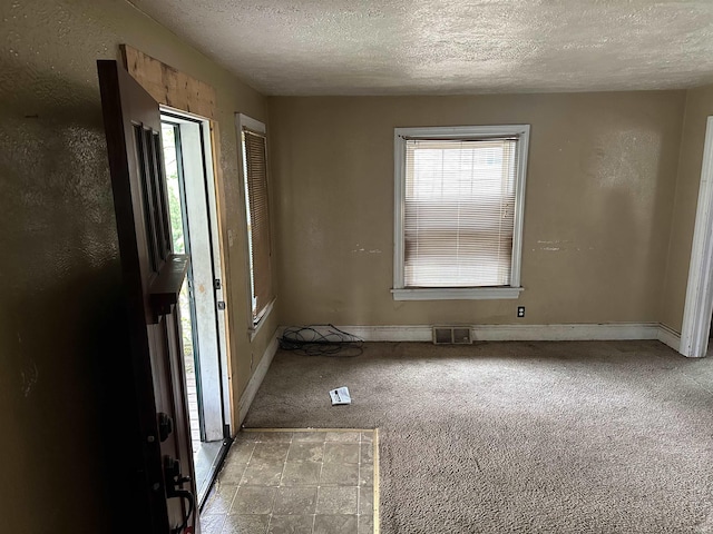 unfurnished room with a textured ceiling, carpet floors, and baseboards