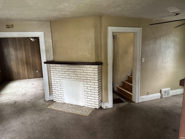unfurnished living room with carpet, a textured ceiling, stairway, a textured wall, and a fireplace
