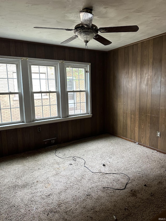 spare room featuring carpet flooring, wood walls, and ceiling fan