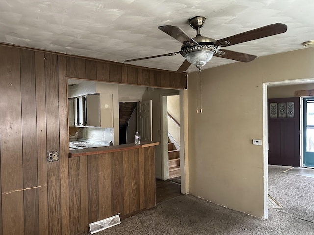 kitchen featuring carpet, wooden walls, and a ceiling fan