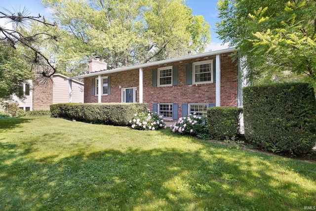 split foyer home featuring a chimney, brick siding, and a front yard