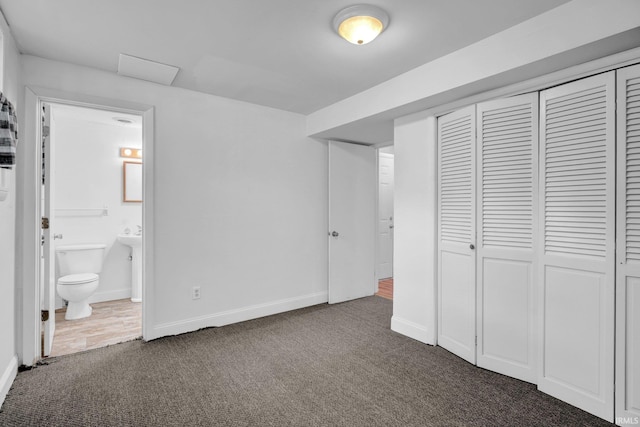unfurnished bedroom featuring dark carpet, a closet, ensuite bath, and baseboards