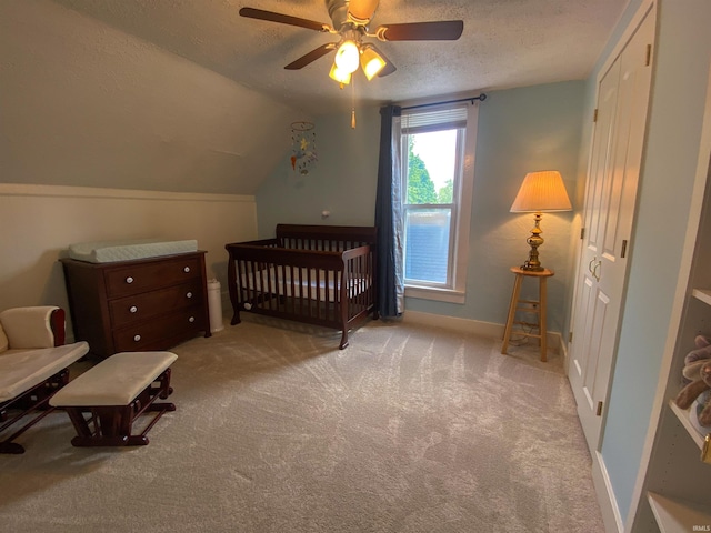 bedroom featuring a textured ceiling, carpet floors, a nursery area, lofted ceiling, and ceiling fan
