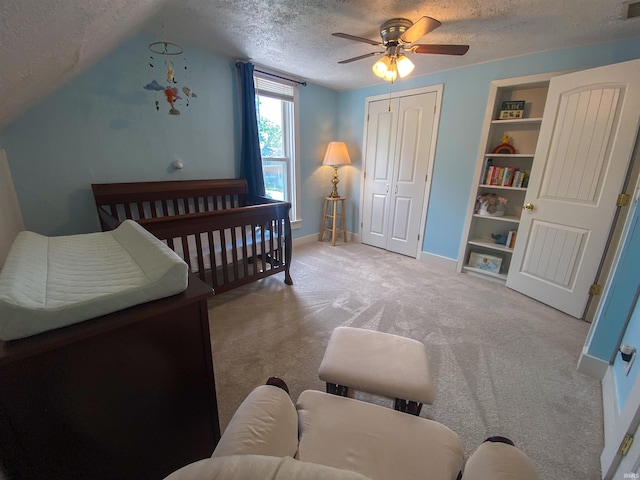 carpeted bedroom with a textured ceiling, baseboards, a closet, a ceiling fan, and a crib