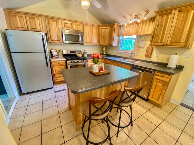 kitchen with stainless steel appliances, a sink, vaulted ceiling, light tile patterned floors, and dark countertops