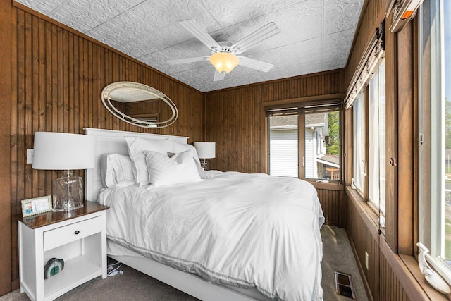 bedroom with dark colored carpet, wooden walls, an ornate ceiling, and a ceiling fan