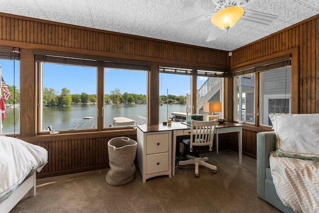 carpeted bedroom with multiple windows, a water view, wooden walls, an ornate ceiling, and a desk