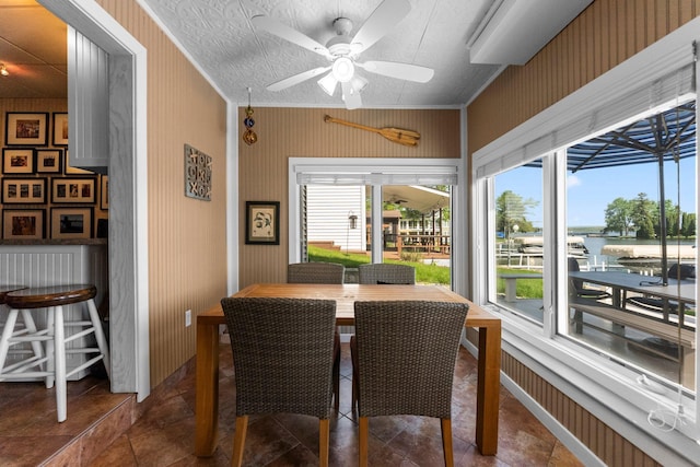 dining room featuring plenty of natural light, a water view, a ceiling fan, wallpapered walls, and ornamental molding