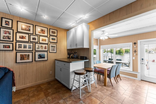 kitchen featuring track lighting, wooden walls, dark countertops, ceiling fan, and baseboards