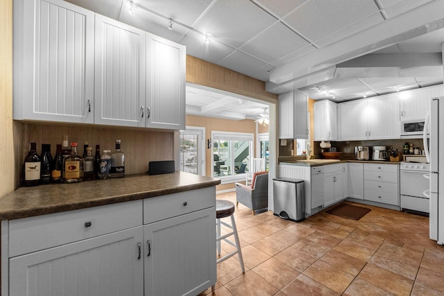 kitchen with white appliances, rail lighting, decorative backsplash, white cabinetry, and a breakfast bar area