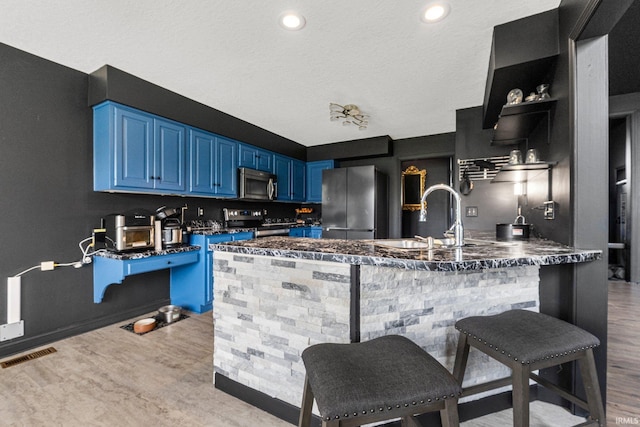 kitchen with appliances with stainless steel finishes, blue cabinets, a sink, light wood-style flooring, and a peninsula