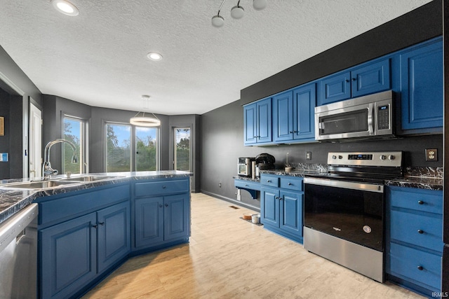 kitchen featuring appliances with stainless steel finishes, a sink, blue cabinetry, dark countertops, and a textured ceiling