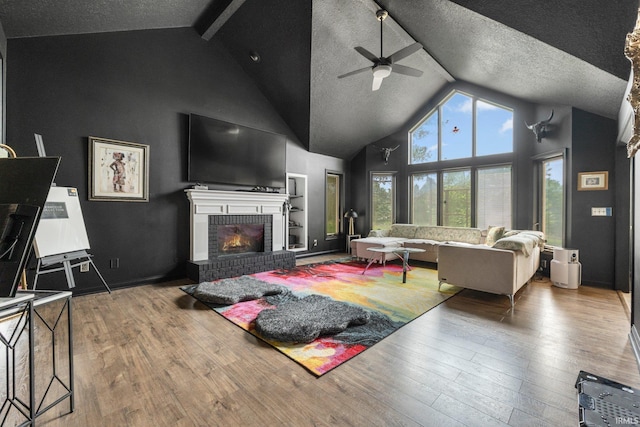 living area featuring a ceiling fan, high vaulted ceiling, hardwood / wood-style floors, a fireplace, and beamed ceiling