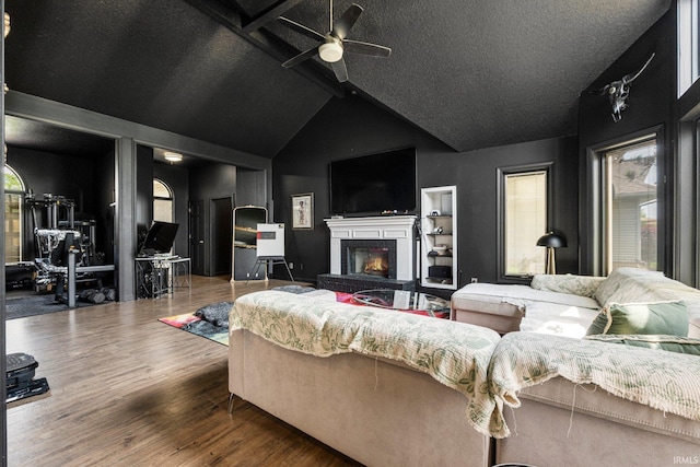 living area featuring a ceiling fan, a fireplace, vaulted ceiling, a textured ceiling, and wood finished floors