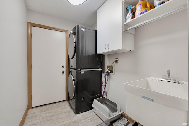 laundry area featuring cabinet space, stacked washer / dryer, light wood-style floors, and baseboards