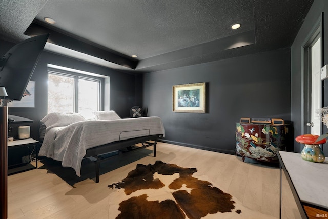 bedroom featuring a tray ceiling, wood finished floors, a textured ceiling, and recessed lighting