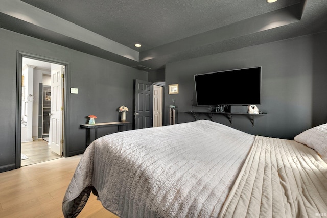 bedroom with a tray ceiling, wood finished floors, recessed lighting, baseboards, and a textured ceiling