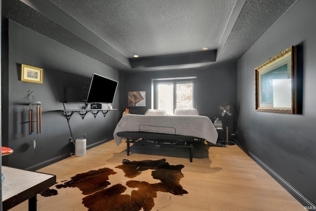 bedroom featuring a textured ceiling, a tray ceiling, wood finished floors, and baseboards