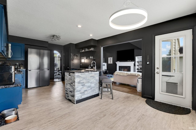 kitchen with freestanding refrigerator, dark countertops, light wood-type flooring, a breakfast bar, and open shelves