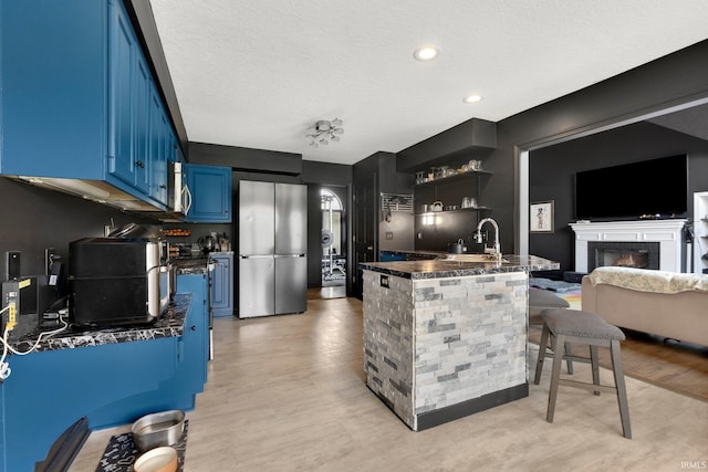 kitchen featuring blue cabinetry, stainless steel appliances, a sink, light wood finished floors, and a kitchen bar