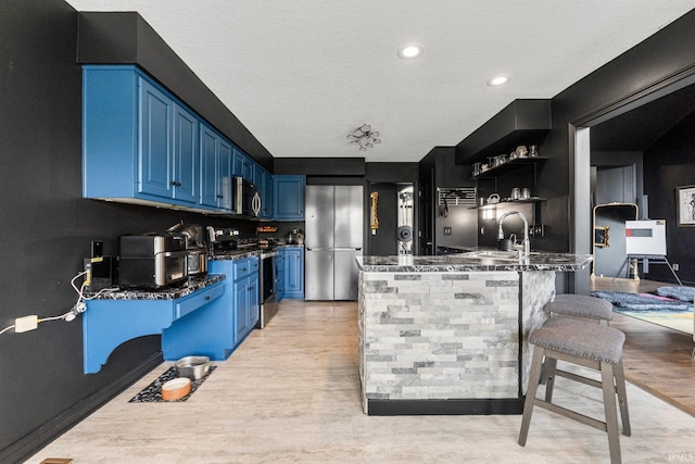 kitchen featuring appliances with stainless steel finishes, blue cabinetry, a sink, a peninsula, and light wood-style flooring