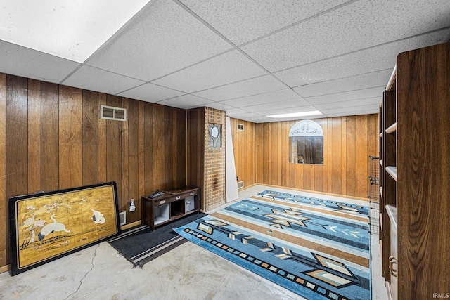 unfurnished room with wooden walls and a drop ceiling