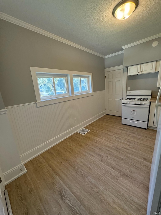 unfurnished bedroom featuring wainscoting, a textured ceiling, wood finished floors, and ornamental molding
