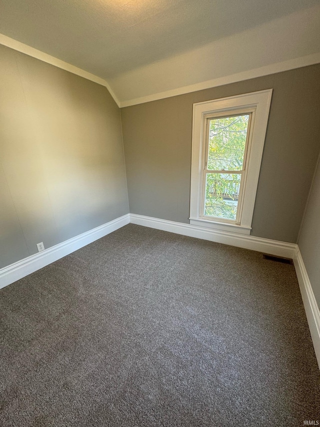 empty room featuring dark colored carpet, baseboards, and vaulted ceiling