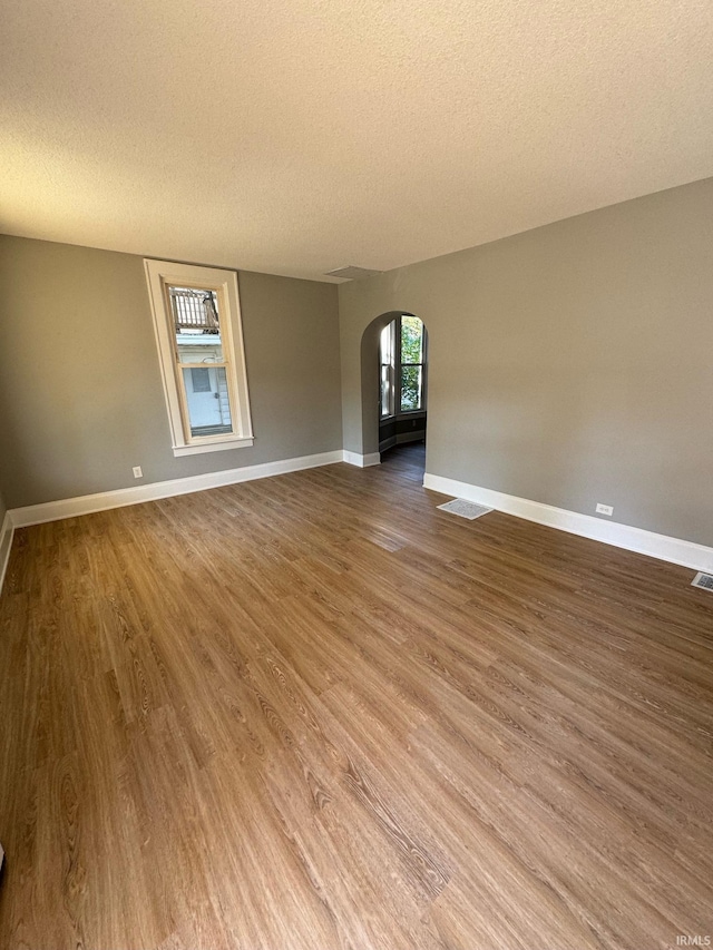 empty room with arched walkways, a textured ceiling, wood finished floors, and baseboards