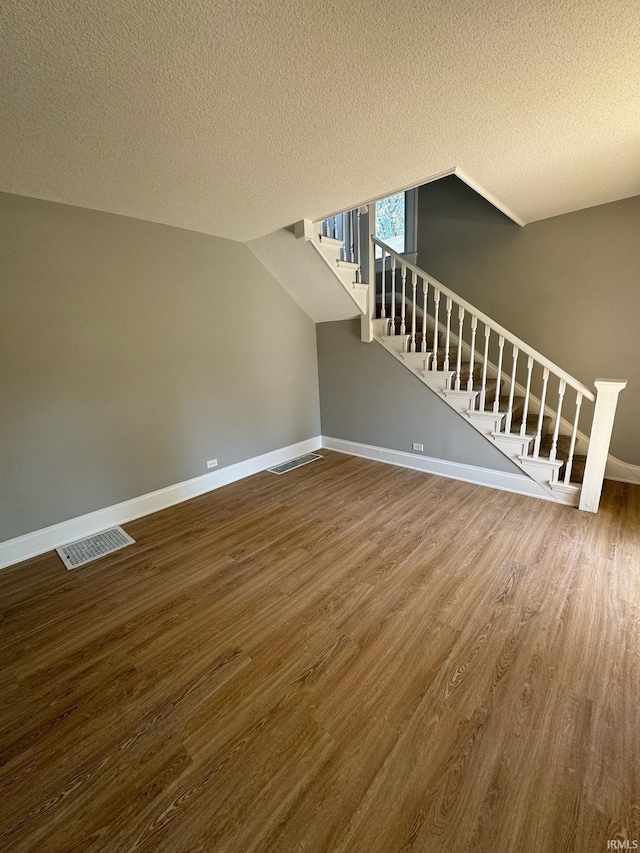 unfurnished living room featuring stairs, wood finished floors, a textured ceiling, and baseboards
