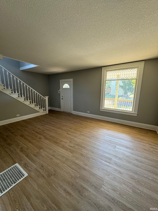 foyer with stairs, wood finished floors, a textured ceiling, and baseboards