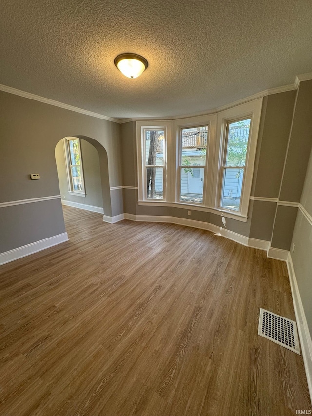 unfurnished room with arched walkways, a textured ceiling, wood finished floors, crown molding, and plenty of natural light