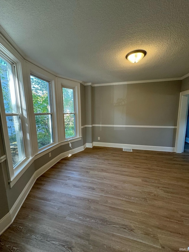 unfurnished room with a textured ceiling, wood finished floors, baseboards, and crown molding