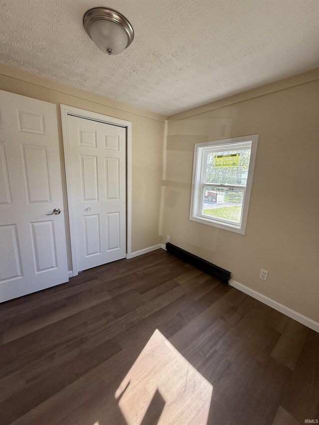 205 W New St, Attica, IN 47918 - unfurnished bedroom with a closet, dark wood finished floors, a baseboard radiator, a textured ceiling, and baseboards