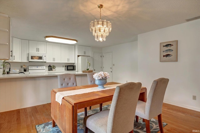 dining space featuring light wood finished floors, a chandelier, and baseboards