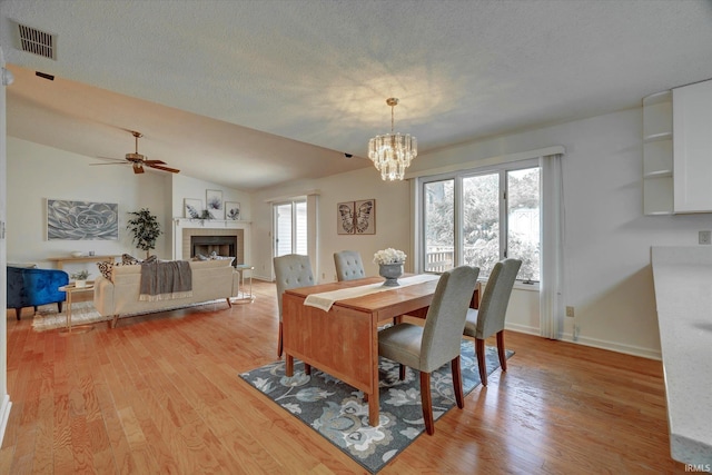 dining room featuring light wood finished floors, a tiled fireplace, a chandelier, a ceiling fan, and baseboards
