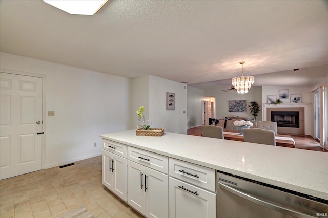 kitchen featuring stainless steel dishwasher, open floor plan, a fireplace, a chandelier, and white cabinetry