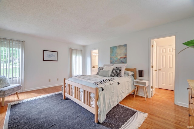 bedroom with light wood-style floors, baseboards, and a textured ceiling