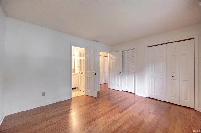 unfurnished bedroom with two closets, light wood-style flooring, baseboards, and connected bathroom
