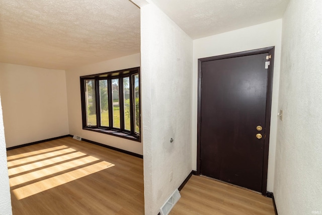 entrance foyer featuring light wood-style flooring, a textured wall, baseboards, and a textured ceiling